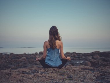 Arkadan Görünüş genç kadının günbatımı meditasyon, denizin kenarında buzlu oturuyor