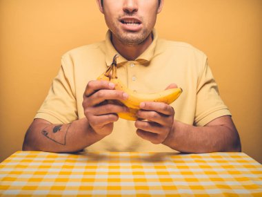 Genç bir adam biraz muz ile sarı bir zemine oturuyor