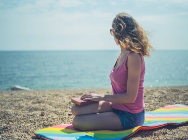 Genç bir kadın bir güneşli yaz günü sahilde oturuyor ve bir kitap okuma