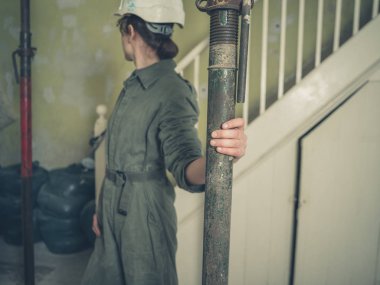 Kask ve bir kazan takım elbise giyen genç bir kadın bir evde tavan destekleyen bazı acro sahne inceliyor