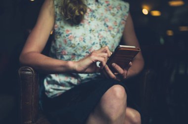 Genç bir kadın bir kafe bir koltukta oturan ve onun smartphone kullanarak