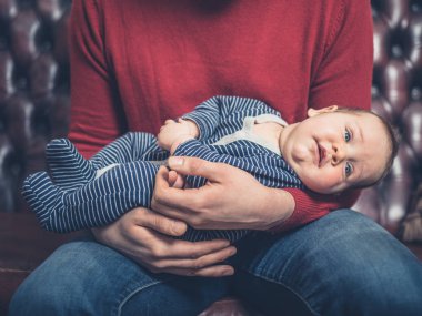 Genç bir baba küçük bebeği ile kanepede oturuyor