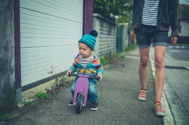 Bir anne bir üç tekerlekli bisiklet sürme onu toddler yanındaki sokakta yürürken