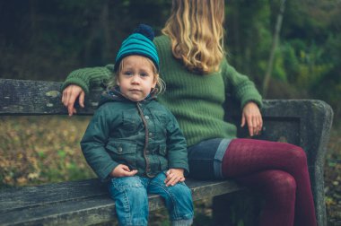 Genç bir anne ve onu yürümeye başlayan çocuk ormanda bir bankta oturuyor
