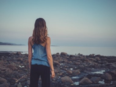 Genç bir kadın batımında sahilde duruyor