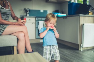 Küçük bir bebek ve annesi mutfakta karpuz yiyor