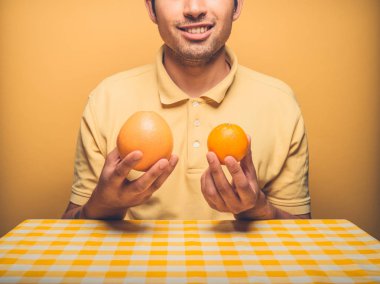 Bir masada oturan genç bir adam bir greyfurt portakal için karşılaştırma