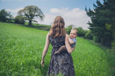 Genç bir anne bebeği ile çim alanlarında duruyor