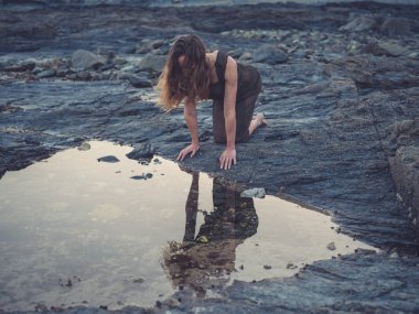 Genç bir kadın batımında sahilde bir rock havuza oturuyor