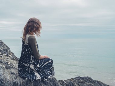 Genç bir kadın bazı kayalar denizin kenarında oturuyor