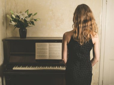 A beautiful young woman in a dress is standing by a piano clipart