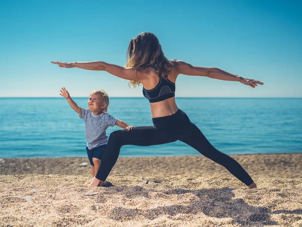 A young mother is doing yoga on the beach with her toddler