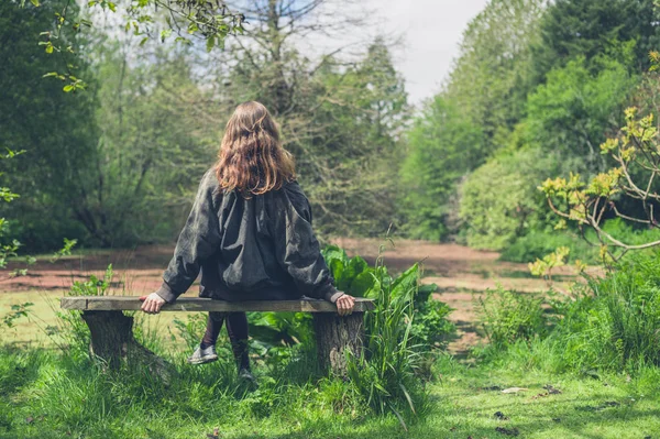 一个年轻的女人坐在池塘边的长凳上 — 图库照片