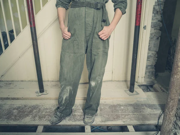 一个穿着锅炉服的年轻人站在正在装修的房子里 — 图库照片