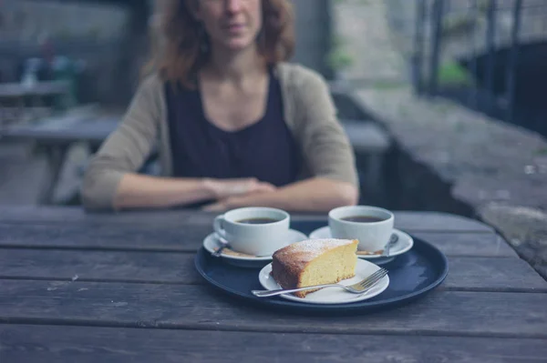 若い女性は外のテーブルでコーヒーとケーキを持ってください — ストック写真