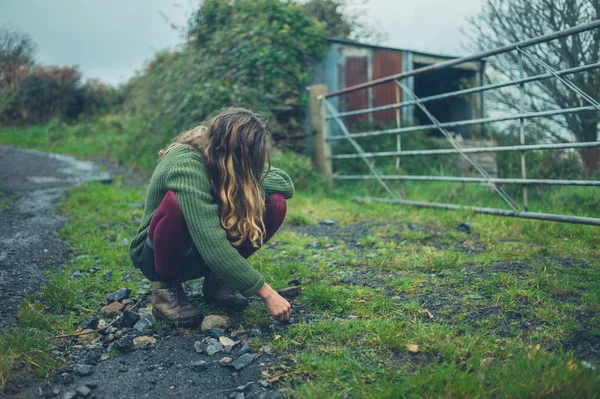 一个年轻的女人正坐在农场旁边的路上 — 图库照片