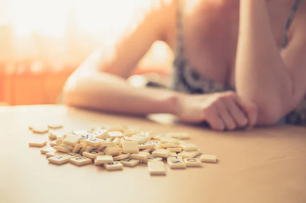 一个年轻的女人坐在一张桌子旁 拿着一堆字母进行文字游戏 — 图库照片