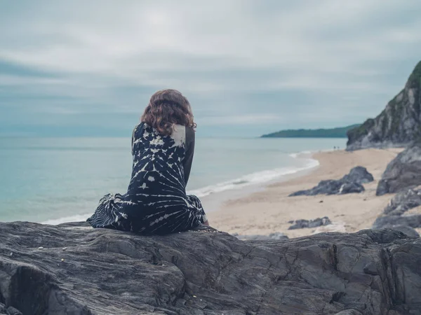 若い女性が海でいくつかの岩の上に座っています — ストック写真