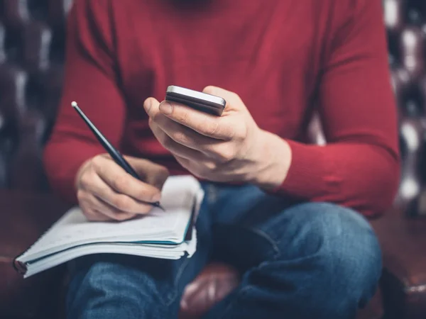Hombre Está Sentado Sofá Usando Teléfono Inteligente Escribiendo Cuaderno —  Fotos de Stock