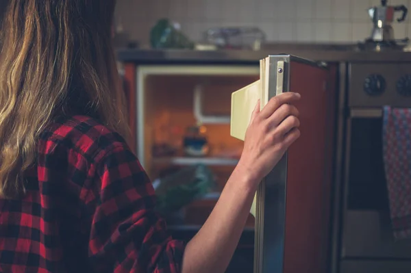 一个年轻的女人正在打开她冰箱的门 — 图库照片