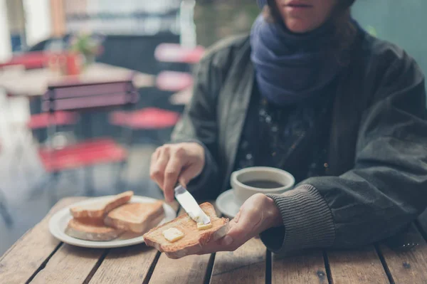 一个年轻的女人在咖啡馆里 正在涂烤面包 — 图库照片