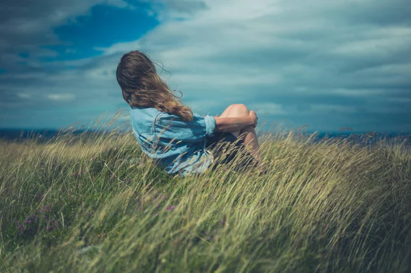 Genç Bir Kadın Bir Alanda Rüzgarlı Bir Günde Oturuyor — Stok fotoğraf