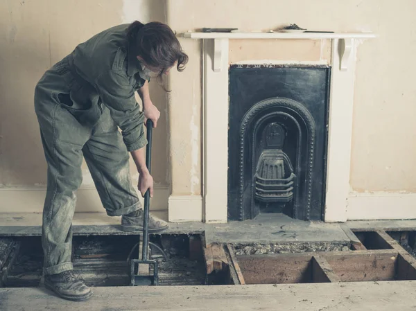 A young woman wearing a boiler suit is taken up the floor boards in a Victorian house