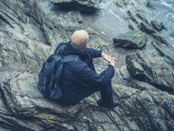 一位资深人士正坐在海边的岩石上 — 图库照片