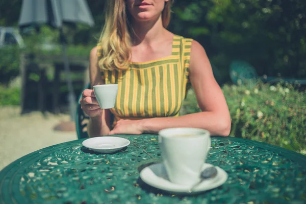 A young woman is drinking coffee outside in a garden in the summer