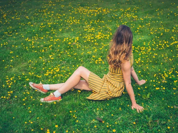ドレスを着ている若い女性は夏に牧草地のキンポウゲの中で座っています — ストック写真