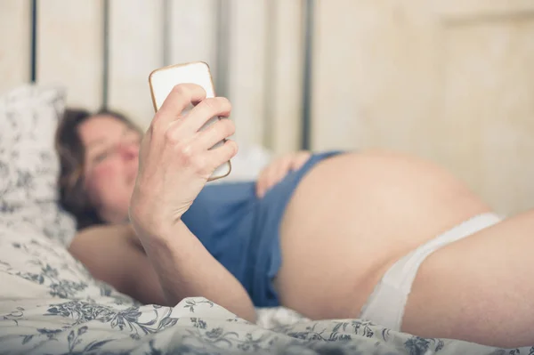 Genç Hamile Kadın Bir Akıllı Telefon Ile Evde Yatakta Yatıyor — Stok fotoğraf