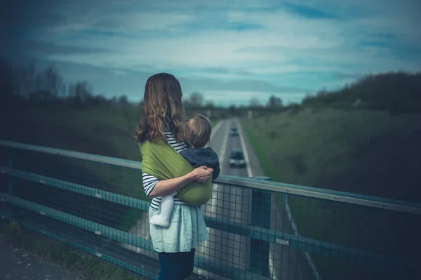 Una Joven Madre Sosteniendo Hijo Cabestrillo Está Pie Puente Sobre —  Fotos de Stock