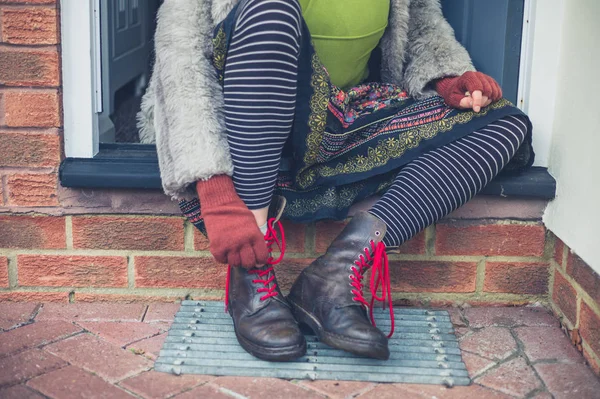 一个年轻的女人正在把靴子绑在屋外的台阶上 — 图库照片