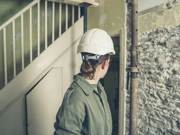 一位戴着硬帽 穿着锅炉服的年轻女子站在一所正在装修的房子里 — 图库照片