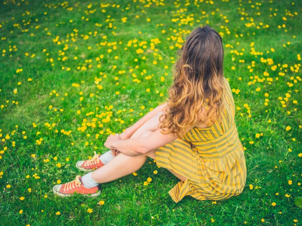ドレスを着ている若い女性は夏に牧草地のキンポウゲの中で座っています — ストック写真