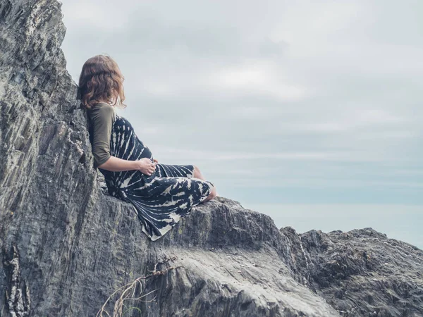 一个年轻的女人坐在海边的岩石上 — 图库照片