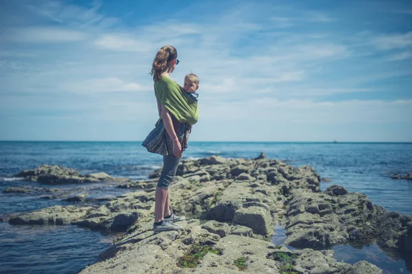 若い母親はスリングで赤ちゃんと海岸を歩いています — ストック写真