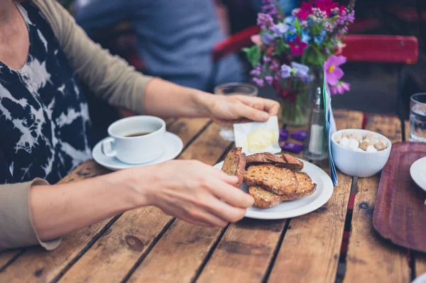 若い女性がカフェでトーストとコーヒーのカップを持つ — ストック写真