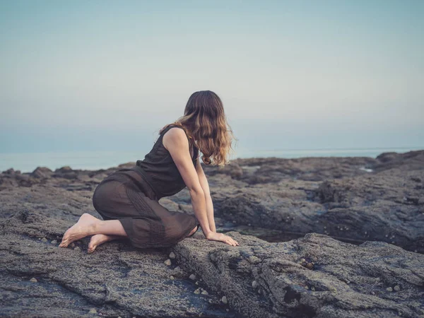 日落时 一位年轻女子坐在海岸的岩石池旁 — 图库照片