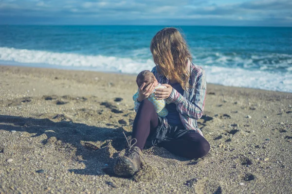 一位年轻的母亲正和她的孩子坐在海滩上 — 图库照片