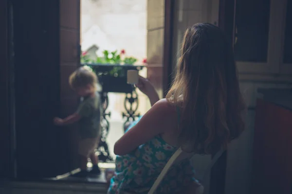 一位母亲一边享受着一杯咖啡 一边看着幼儿在阳台上玩耍 — 图库照片