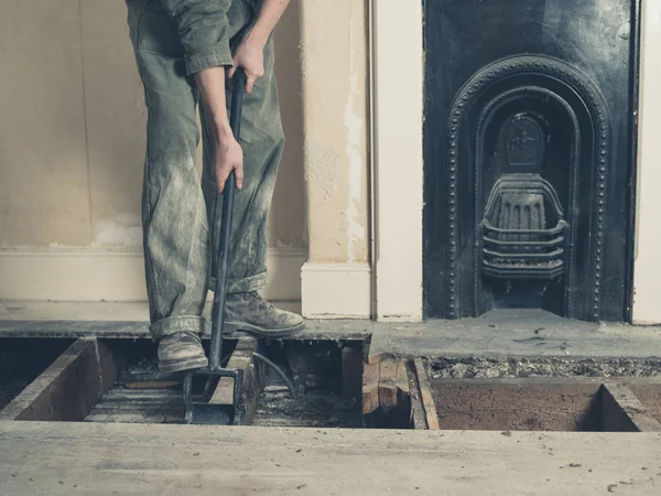 A young woman wearing a boiler suit is taken up the floor boards in a Victorian house