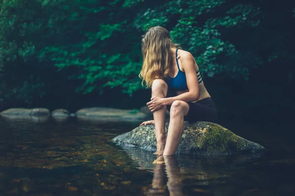 一位年轻女子正坐在河里放松的岩石上 — 图库照片