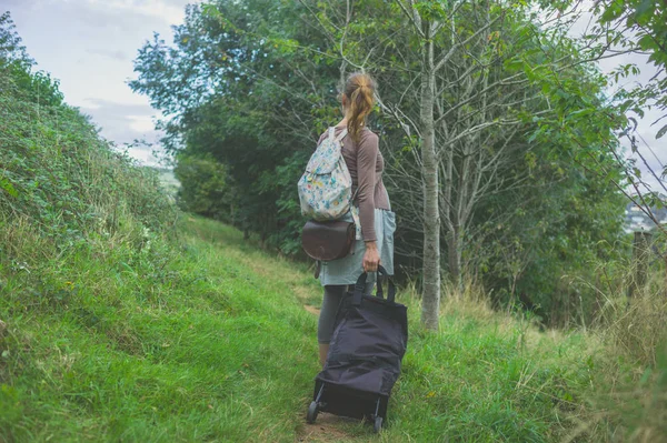 A young woman with luggage is walking in the countryside