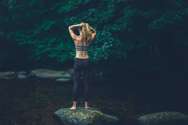 一个年轻的健身女子站在河边的一块岩石上 — 图库照片