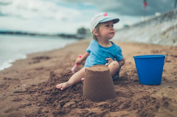 Uma Criança Pequena Está Sentada Praia Com Balde Castelo Areia — Fotografia de Stock