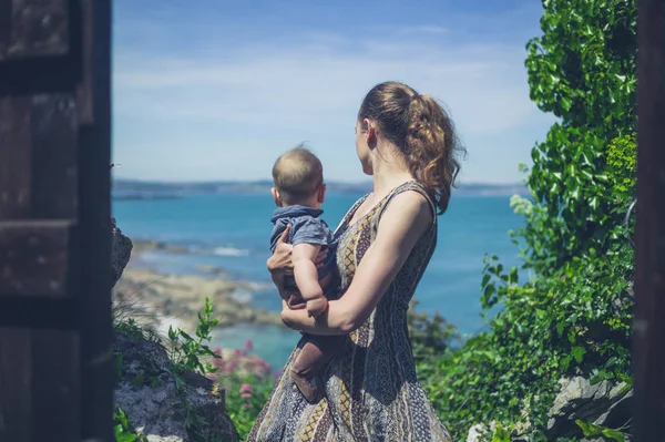 一位年轻的母亲带着她的小宝宝站在海边 — 图库照片