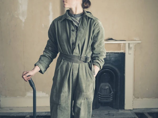 ボイラー スーツを着た若い女性が彼女の手にバールでビクトリア朝の家の暖炉のそばで立っています — ストック写真