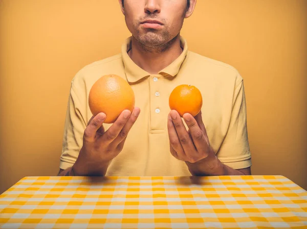 坐在桌旁的一个年轻人正在把葡萄柚比作橘子 — 图库照片