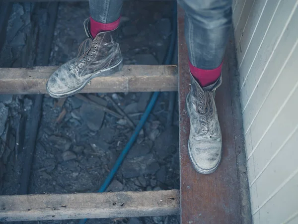 家の改装工事で床の梁の上に立って汚い古いブーツを身に着けている労働者の足 — ストック写真
